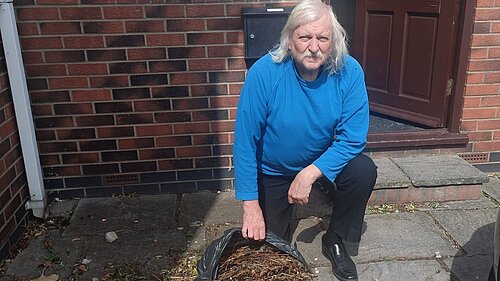 Councillor Tony Fisher kneeling by a bag of garden waste which was dumped at his home