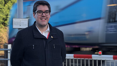 Ed Pearson standing by a level crossing as a train passes behind